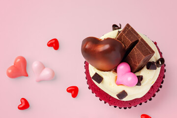 Valentine red cupcake decorated with heart chocolate and pink heart on pink background, celebrating love concept