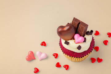 Valentine red velvet cupcake decorated with heart chocolate and heap of hearts on light brown background, celebrating love concept