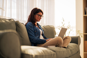 Obraz premium Woman working comfortably on laptop at home sofa