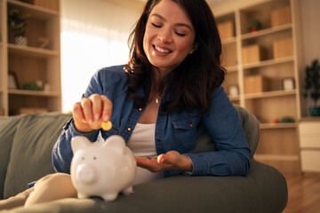 Woman saving money in piggy bank at home