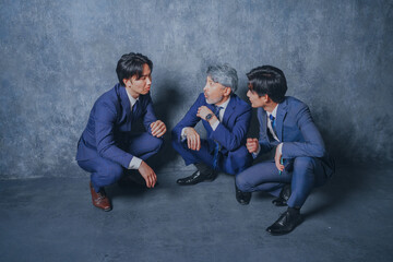 座り込んで噂話をするスーツ姿のビジネスマン3人
