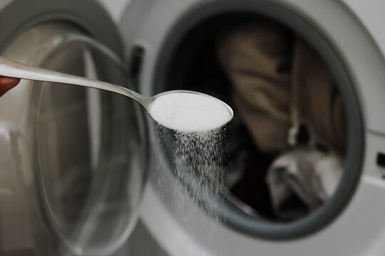 Spoon with salt in front of a washing machine. Stain removal, color fixing, odor control, and eco-friendly washing concept. Home cleaning hacks.