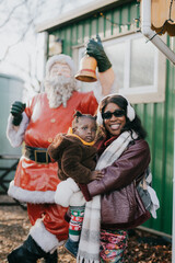 A woman and a child are posing in front of a Santa Claus statue. The woman is wearing a red jacket and the child is wearing a brown jacket. Scene is festive and joyful, as the woman