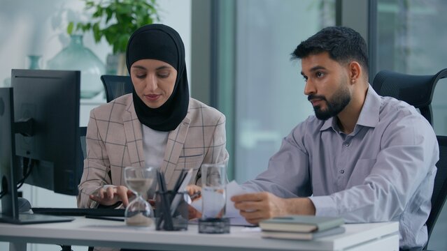 Two muslim hindu business team in office working Islamic group Indian co-workers Arabian colleagues work with computer online startup data paper document talking boss man businessman help woman intern