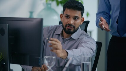 Business team in office working together talking two Indian Arabian Saudi Muslim businesspeople colleagues discuss job project with computer at table talk cooperation startup research development
