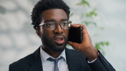 Angry mad African American business man yelling arguing talking mobile phone holding papers in office work documents mistake ethnic businessman male furious argument quarrel conflict smartphone call