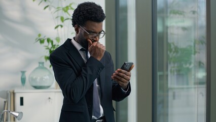 African American businessman looking serious at smartphone reading bad news texting using mobile phone business man sad male professional in office worried about message digital communication stress