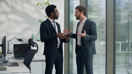 Two multiracial businessmen emotional discussing startup in office holding at digital tablet business men diverse male colleagues talking cooperation teamwork corporate friendship sharing news ideas