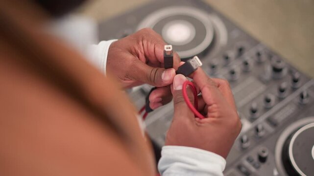 hands plugging audio cable into controller outdoor street setup with red coiled cable closeup of hands adjusting connector focused anticipation before set dj equipment and deck in shallow depth