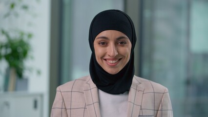 Portrait in office happy smiling toothy Arabian ethnic Muslim business woman looking at camera smile carefree Indian Islamic businesswoman satisfied posing in company wearing hijab female girl working