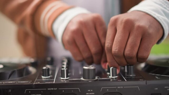 Closeup black DJ hands mixing controller, street busking scene with warm bokeh, tactile knob and fader adjustments, casual jacket sleeves, daytime outdoor set, immersive groove and concentrated
