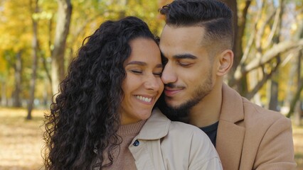 Hispanic couple cuddling in autumn park touching faces cheeks smiling enjoy tenderness closeness diverse girl and guy in love hugging romantic date married Arabian husband wife cuddle hug smile family