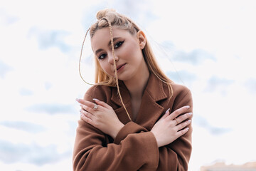 Influencer with braids hairstyle and brown coat is posing with arms crossed on a cloudy day, showcasing her unique style and confidence for social media content
