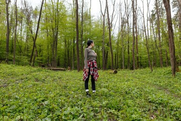 Young woman hiker wearing casual clothing enjoying peaceful walk in vibrant green forest during springtime, embracing tranquility of nature