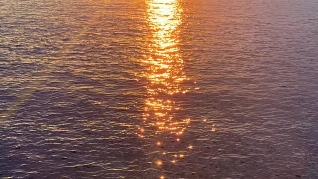 The shimmering rays of the setting sun reflect off the surface of the water, everything is illuminated with orange light and glare.