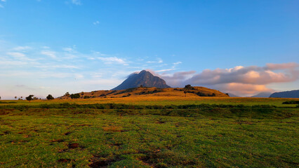 a view of a meadow at sunrise with a towering mountain in the background