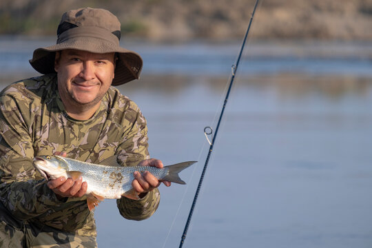 A fisherman holds a fish in front of a pond. A caught asp.