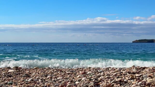 A serene beach scene with gentle waves crashing onto the pebbly shore, with buoys in the water to mark the safe area