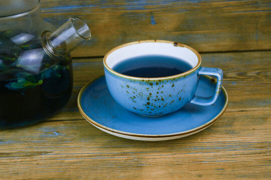 Refreshing blue  tea in cup and teapot on grey wooden table against gray background