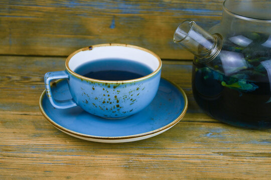Refreshing blue  tea in cup and teapot on grey wooden table against gray background