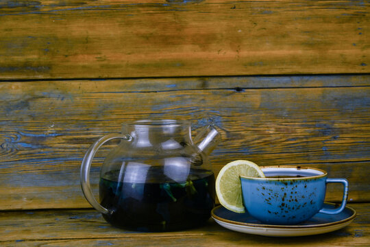 Refreshing blue  tea in cup and teapot on grey wooden table against gray background
