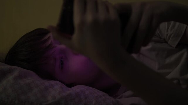 Close-up of a 12-year-old Caucasian preteen boy using a smartphone in bed at night after waking up in the dark