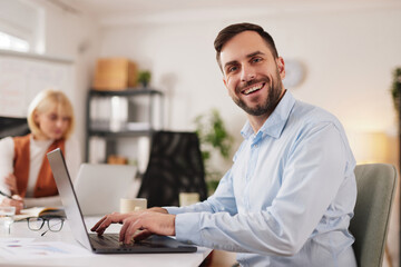 Team members work together on a project in a bright office space, sharing ideas and discussing tasks while using laptops and writing notes at a large table.