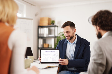 Obraz premium A man shows a tablet to his colleagues during a meeting in an office. They collaborate on plans and share ideas to achieve success.