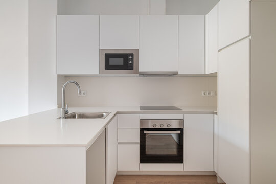 Modern kitchen with white cabinets, stainless steel appliances, and a minimalist design. Features a sink, microwave, and oven.