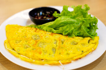 Traditional Vietnamese crispy pancakes called Banh Xeo, served with fresh salad and sauce on a white plate