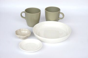 Minimal ceramic tableware set including two matte green mugs, white bowl, small plate and textured dipping bowl isolated on white background. Modern kitchenware concept for dining, home decor and life
