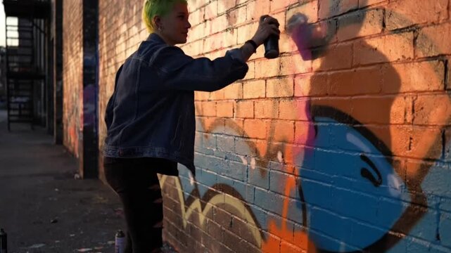 Young artist with green hair spray painting vibrant graffiti on a brick wall