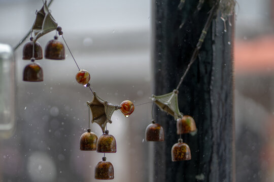 Rainy season in Asia. Traditional decorative hanging wind chimes swaying in rain, close-up detail. Soft bell sounds symbolize protection, harmony. Rainy weather, outside decor, blurred background. 