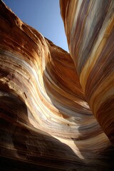 Obraz premium Curved sandstone layers reveal warm earth tones under a clear sky.