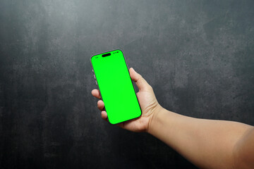 Hand holding smartphone with green screen on dark background. Concept of mobile app mockup, digital marketing, UI presentation, advertising, and technology promotion.