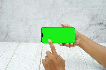 Hand holding smartphone with green screen in landscape orientation on light wall background. Concept of mobile mockup, video ads, app demo, digital marketing, and screen replacement.