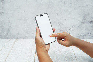 Two hands holding smartphone with blank white screen on bright wooden desk and light wall background. Concept of mobile mockup, app interaction, UI UX presentation, and digital marketing.