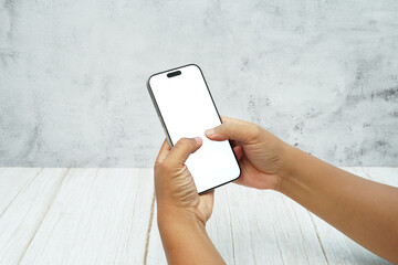 Two hands holding smartphone with blank white screen on bright wooden desk and light wall background. Concept of mobile mockup, app interaction, UI UX presentation, and digital marketing.