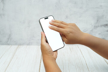 Two hands holding smartphone with blank white screen on bright wooden desk and light wall background. Concept of mobile mockup, app interaction, UI UX presentation, and digital marketing.