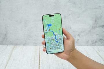 Hand holding smartphone displaying generic map and navigation interface for location tracking and route planning.