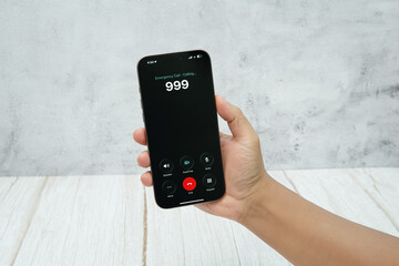 Hand holding smartphone showing an emergency call interface with number 999 on the screen.