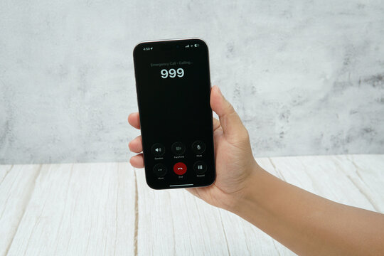 Hand holding smartphone showing an emergency call interface with number 999 on the screen.