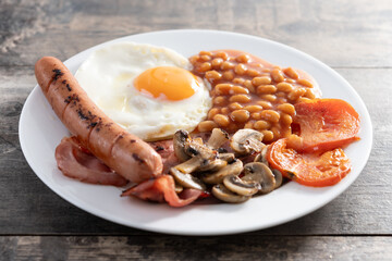 Full English breakfast with fried egg, bacon, sausages and beans on wooden table