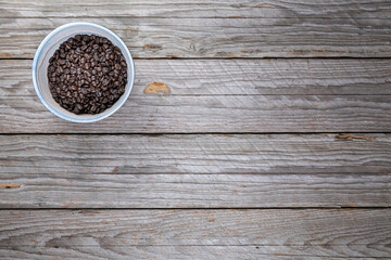 Top view ceramic bowl with roasted coffee beans on weathered wood
