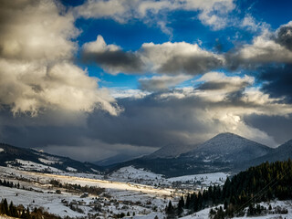 Mystical snowy Carpathian peaks under cloudy skies in the sunny weather