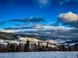 Mystical snowy Carpathian peaks under cloudy skies in the sunny weather