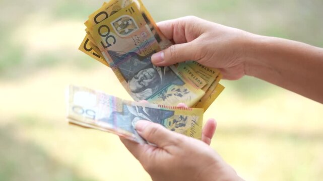 Hands counting and exchanging Australian dollar banknotes, symbolizing cash payment, financial transaction, personal finance, economy, savings, and everyday money exchange.