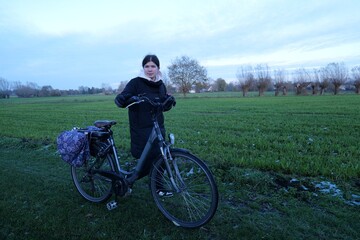 Obraz premium Woman with bicycle stands in field on a winter morning