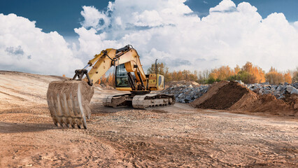 A powerful excavator is at work at a construction site, moving soil and rocks. Trees are visible in...