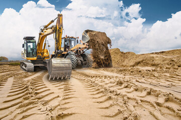 Obraz premium Deep tracks on sandy ground show the work of heavy machinery at a construction site. Sand piles rise in the background as the work continues under clouds